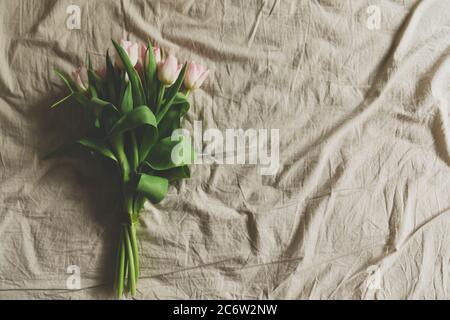 Auf einem zerknittert liegenden Bett liegen rosa Tulpen. Frühlingshintergrund in warmen Farben. Stockfoto