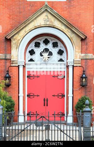 Rote vintage gewölbte hölzerne Eingangstür mit schwarzen Griffen und dekorativen Scharnieren, weißen Säulen und Zierleisten und Kalksteinportal. New Jersey. USA. Stockfoto