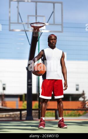 Portrait des jungen afroamerikanischen Sportlers mit Basketball im Freiluftstadion Stockfoto