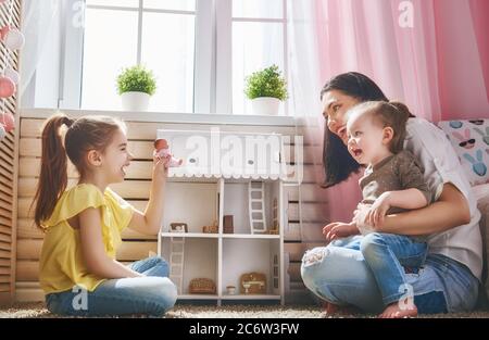 Glückliche Mutter und Töchter Mädchen spielen mit Puppenhaus zu Hause. Lustige, nette Familie haben Spaß im Kinderzimmer. Stockfoto