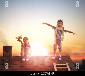 Zwei kleine Kinder spielen auf dem Dach des Hauses und schauen in den Himmel und träumen davon, Pilot zu werden. Stockfoto