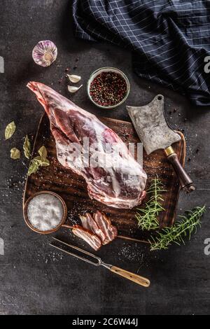 Rohes Lammkeule, umgeben von Salz, Pfeffer, Knoblauch, Speck und Rosmarin auf einer Vinategoberfläche Stockfoto