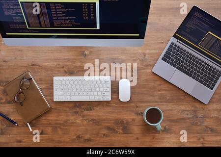Top-Down-Ansicht an einem modernen Arbeitsplatz mit zwei Computern und Kaffeetasse auf einem strukturierten Holztisch, Kopierfläche Stockfoto