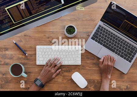 Draufsicht auf männliche Hände, die am modernen Arbeitsplatz auf der Tastatur tippen, mit Computern und Kaffeetasse auf einem strukturierten Holztisch, Platz zum Kopieren Stockfoto