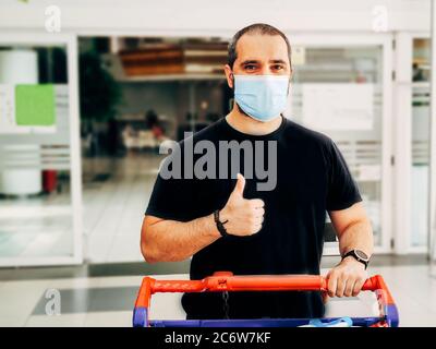 Mann in medizinischer Maske beim Einkaufen im Supermarkt mit Daumen nach oben. Stockfoto