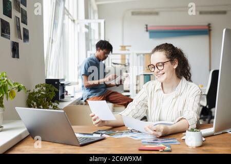 Portrait der jungen Frau Überprüfung von Fotografien während der Arbeit an der Bearbeitung und Veröffentlichung in modernen Büro, Copy Space Stockfoto