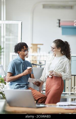 Vertikales Porträt zweier kreativer junger Menschen, die sich in der Kaffeepause im modernen Büro Fotos angeschaut und chattet Stockfoto