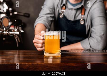 Freundlicher Barkeeper. Der Mann im Vorfeld legt einen Becher Bier auf die Holztheke im Innenraum