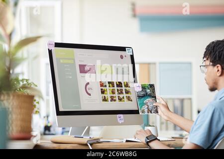 Porträt des jungen afroamerikanischen Fotografen Verwaltung Foto-Stock-Marktplatz, während mit Computer am Schreibtisch im Home Office mit Foto-Website auf SCR Stockfoto