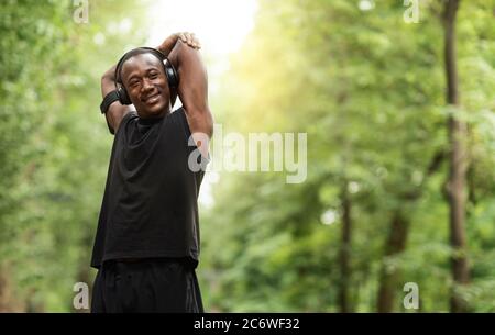 Lächelnder afrikanischer Mann, der sich vor dem Joggen im Park ausdehnt Stockfoto