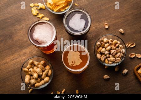 Dunkles, helles, ungefiltertes Bier im Glas auf Holztisch mit Snacks auf Tellern Stockfoto