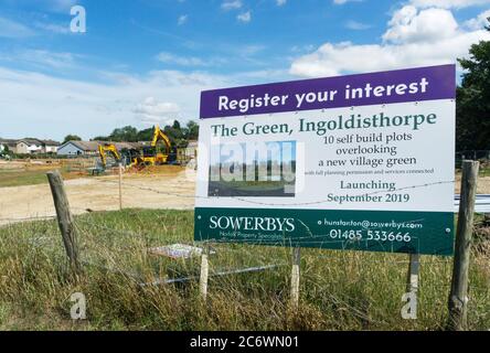 Immobilienmakler Zeichen für selbst bauen Wohngrundstücke zum Verkauf in einer Neuentwicklung rund um ein Dorf grün in Ingoldisthorpe, West Norfolk. Stockfoto