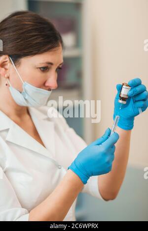 Ärztin zieht eine Lösung in eine Spritze aus einer Ampulle - Impfung - Vorbereitung einer Injektion Stockfoto