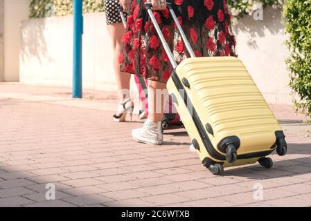 Von unten zugeschnittenes Foto von zwei eleganten Touristenfrauen, die mit Koffern auf der blumigen Straße der Stadt spazieren. Stockfoto
