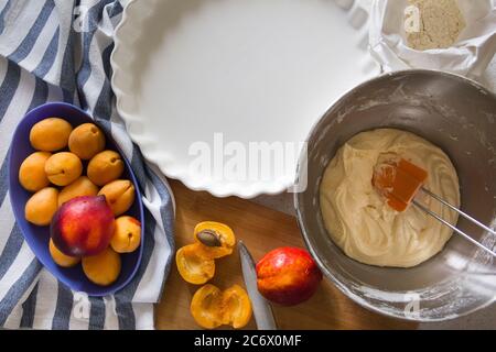 Prozess der Herstellung von Aprikose hausgemachten Kuchen. Reife Aprikosen und Nektarinen auf einem Schneidebrett, Teig in einer Metallschale Stockfoto