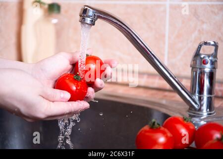Waschen von Gemüse unter dem Schweiß des Wassers in der Spüle. Harte Hände halten saftige rote Tomaten. Hygienekonzept, Zubereitung von Gemüse vor dem Kochen Stockfoto