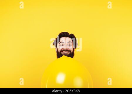 Lächelnder Mann mit aufblasbarem gelben Ballon, Urlaubsmann auf hellem Hintergrund Stockfoto