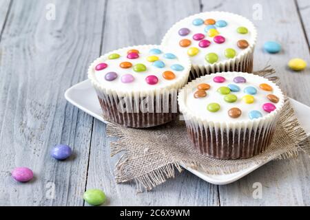 Cupcakes mit weißer Glasur und farbigen Smartys auf dem Teller, Holzhintergrund Stockfoto