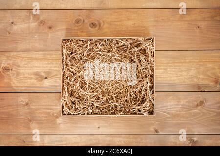 Geöffnete Geschenkbox mit geschreddertem Papier auf Holzhintergrund. Flach liegend, Draufsicht. Karton für den Produktaustausch. Stockfoto