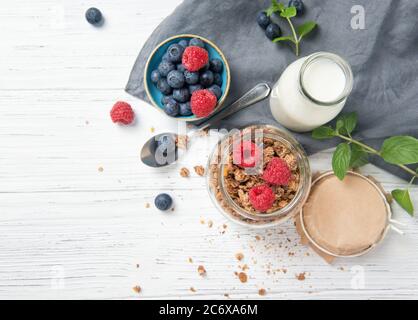 Müsli, Milch und reife Heidelbeeren und Himbeeren, gesundes Frühstückskonzept, Holzhintergrund, Draufsicht Stockfoto