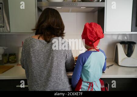 Rückwärts Mutter lehrt Tochter in Red Chef Hut in der Küche Stockfoto