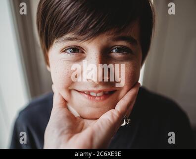 Nahaufnahme des glücklichen Jungen Gesicht unter seinem Kinn durch eine Hand gehalten. Stockfoto