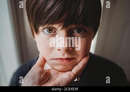 Nahaufnahme des Gesichts des Jungen, das an einer Hand unter seinem Kinn gehalten wird. Stockfoto