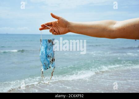 Person am Strand hält eine Mülleimer Gesichtsmaske, die die Wellen auf den Sand gewaschen haben Stockfoto