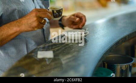 Bar-Kunde hält Tasse Espresso Kaffee Cappuccino Nahaufnahme über Kopf geschossen, Tageslicht, an der Bar, auf einem Tisch, selektive Fokus und Bokeh, flach Stockfoto