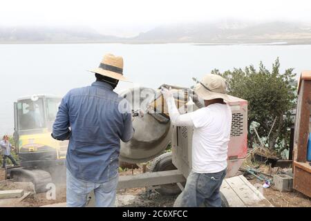 Mexikanische Arbeitskräfte bauen eine Zement Stützmauer mit Blick auf Morro Bay Mündung in Zentral-Kalifornien setzen Zement in Mischer für Fugen Stockfoto