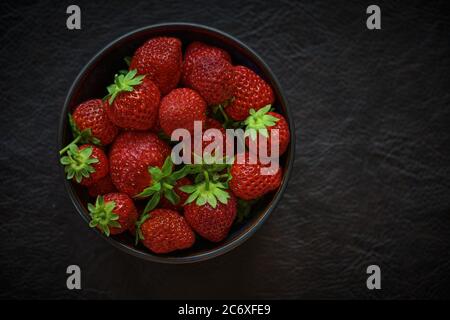 Frische Erdbeeren in dunkler Schüssel. Stockfoto