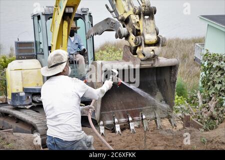 Mexikanische Arbeiter bauen eine Zement Stützmauer mit Blick auf Morro Bay Mündung in Zentral-Kalifornien Waschkübel Traktor Stockfoto