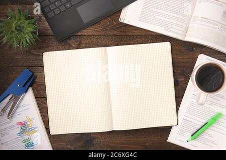 Flacher Schreibtisch mit Schreibtisch und Draufsicht. Arbeitsbereich mit offenen Büchern, Laptop, Bürobedarf, Bleistift, Kaffeetasse und leerem Notizblock auf Holzhintergrund Stockfoto