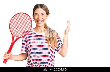 Schöne kaukasische Frau mit blonden Haaren spielen Tennis halten Schläger schreien stolz, feiert Sieg und Erfolg sehr aufgeregt mit erhobenem Arm Stockfoto
