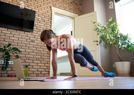 Aktive Frau dabei Plank Übung zu Hause beobachten Online-Video auf Laptop. Stockfoto