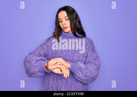 Junge schöne Frau trägt lässige Rollkragenpullover über lila Hintergrund stehend Überprüfung der Zeit auf Armbanduhr, entspannt und zuversichtlich Stockfoto