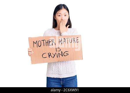 Junge schöne chinesische Frau hält Mutter Natur weint Karton Banner über Mund mit Hand, schockiert und Angst vor Fehler. Überrascht exp Stockfoto