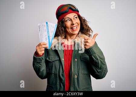 Eine Dame aus dem mittleren Alter trägt eine Skifahrbrille mit der Bordkarte der Fluggesellschaft und zeigt mit dem Daumen nach oben zur Seite mit einem fröhlichen Gesicht Stockfoto