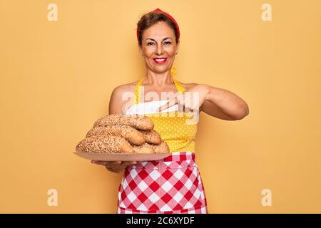 Mittlere Alter Senior Hausfrau Pin up Frau tragen 50s Stil Retro-Kleid Kochen Vollkornbrot sehr glücklich zeigen mit Hand und Finger Stockfoto