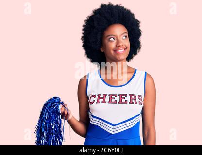 Junge afroamerikanische Frau trägt Cheerleader Uniform hält Pompon lächelnd Blick zur Seite und starrte weg denken. Stockfoto