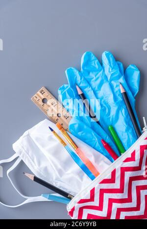 Kinder-Bleistifttasche mit Schulbedarf, OP-Maske und Handschuhen gefüllt. Flach lag auf grauem Hintergrund Stockfoto