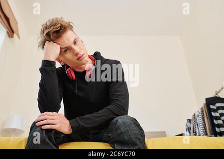 Unglücklicher Student sitzt auf Bettkante in seinem Zimmer und Blick auf Kamera gelangweilt zu Hause während covid-19 Pandemie Stockfoto