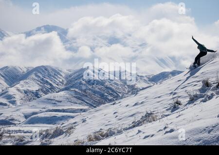 Ein eineinesiger Snowboarder schnitzt während einer Wintertour einen Hügel im Chuy-Gebiet von Kirgisistan hinunter. Stockfoto