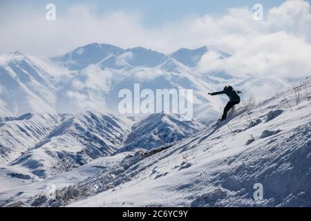 Ein eineinesiger Snowboarder schnitzt während einer Wintertour einen Hügel im Chuy-Gebiet von Kirgisistan hinunter. Stockfoto