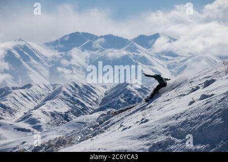 Ein eineinesiger Snowboarder schnitzt während einer Wintertour einen Hügel im Chuy-Gebiet von Kirgisistan hinunter. Stockfoto