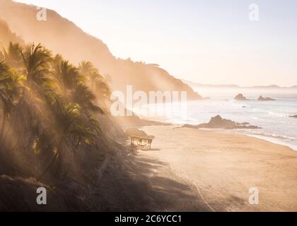 Am frühen Morgen scheint die Sonne durch Palmen am Strand El Calvario an der Costa Grande von Guerrero, Mexiko. Stockfoto