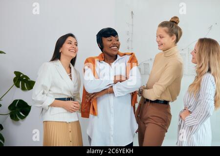 Portrait des erfolgreichen Teams von vier verschiedenen Business-Damen in Casual-Kleidung gekleidet und stehen lächelnd, diskutieren, einander anschauen. Light modernen Bus Stockfoto