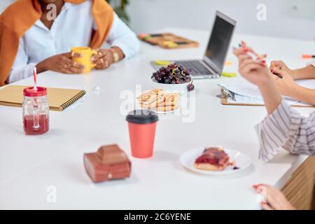 Büroangestellte sitzen während der Pausen und in der Freizeit auf dem Tisch. Tasse Kaffee, Saft, Obst und Kuchen auf dem Tisch Stockfoto