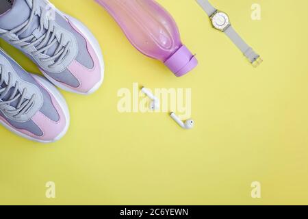 Flache Sportschuhe, Flasche Wasser, Uhr und Kopfhörer auf gelbem Hintergrund. Konzept gesunde Lebensweise, Sport und Ernährung. Speicherplatz kopieren. Stockfoto