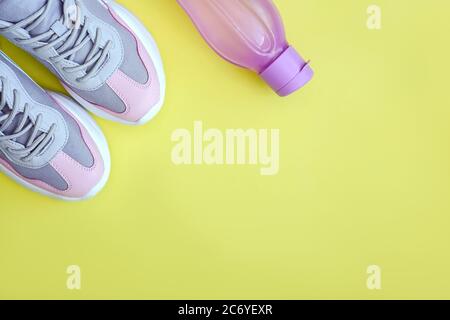Flache rosa Sportschuhe und eine Flasche Wasser auf gelbem Hintergrund. Konzept gesunde Lebensweise, Sport und Ernährung. Speicherplatz kopieren. Stockfoto